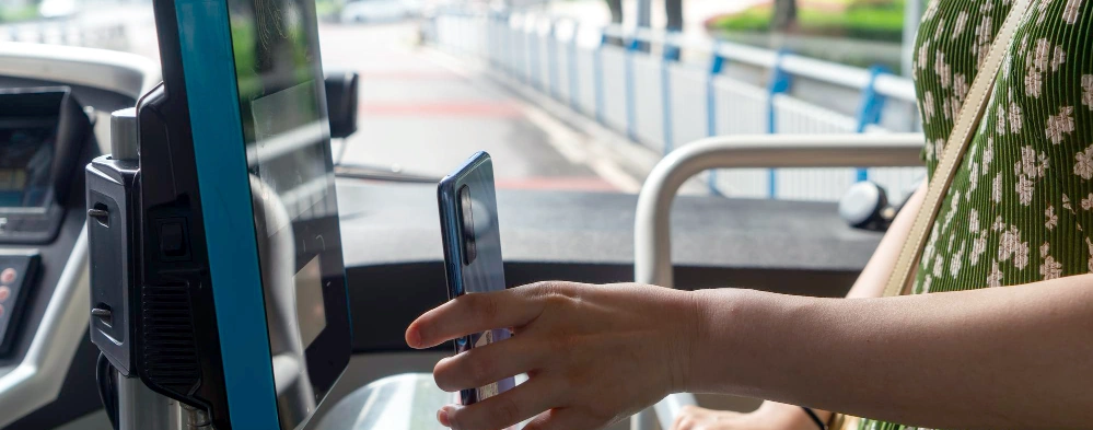 A passenger presents a smartphone fare token to a validator inside a bus.