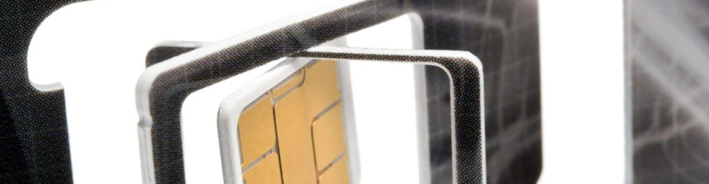 A SIM chip is held by precision tweezers against a dark laboratory background.