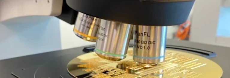 A microscope examines the circuitry of a gold integrated circuit on a laboratory stage.