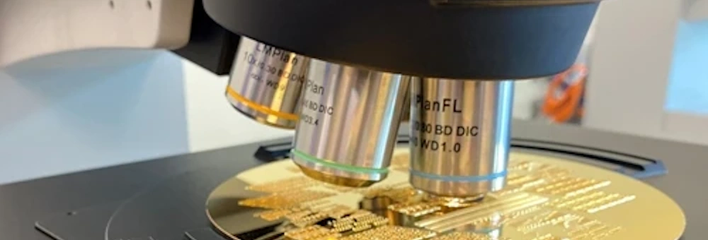 A microscope examines the circuitry of a gold integrated circuit on a laboratory stage.