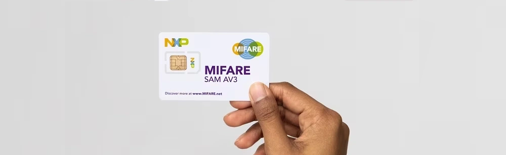 A hand holds a MIFARE SAM AV3 card against a pale neutral background.