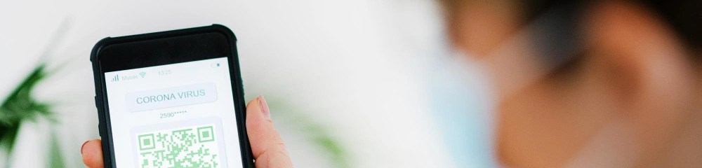 A hand holds a smartphone displaying a health QR code while another person stands out of focus.